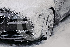 Modern black car covered by foam. Wash high pressure water and soap. Close up of auto on car wash station. Vehicle clean service