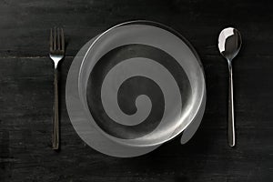 Modern black dining table setting with empty black plate, fork and spoon