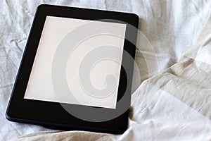 A modern black electronic book with a blank empty screen on a white and beige bed closeup. Mockup tablet on bedding