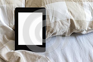 A modern black electronic book with a blank empty screen on a white and beige bed. Mockup tablet on bedding