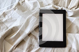 A modern black electronic book with a blank empty screen on a white and beige bed. Mockup tablet on bedding