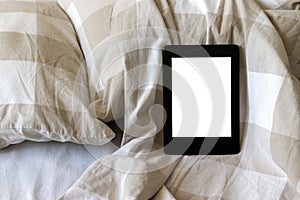 A modern black electronic book with a blank screen on a white and beige bed. Mockup tablet on bedding