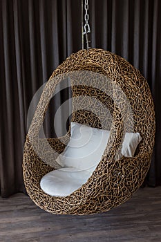 Modern black rattan chair hanging. Hanging chair in room interior. Modern armchair in shape of eggshell or birds nest made of wove