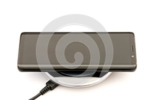 Modern black smartphone charging on wireless charger pad. Isolated on white