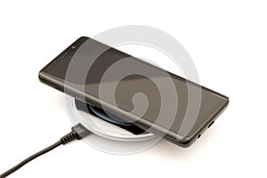 Modern black smartphone charging on wireless charger pad. Isolated on white background.