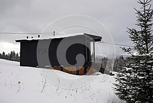 Modern Black wooden cabin in pine forest in snowy weather