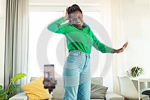 Modern blogging concept. Joyful african american female blogger making video on smartphone, dancing at home
