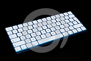 Modern blue aluminum computer keyboard isolated on black background.