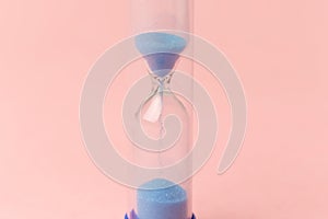 Modern blue Hourglass on pink background. Sand trickling through the bulbs of a crystal sand glass. Symbol of time