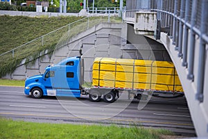 Modern blue semi truck with yellow cover cargo on trailer flat b