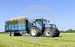 Modern blue tractor pulling a trailer in grass field