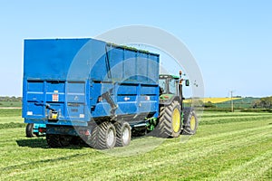 Modern blue tractor pulling a trailer in grass field