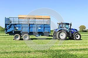 Modern blue tractor pulling a trailer in grass field