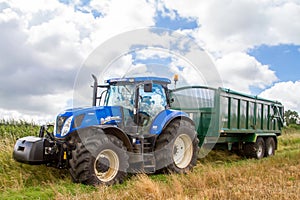 Modern blue tractor pulling a trailer in harvest field