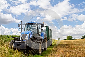 Modern blue tractor pulling a trailer in harvest field