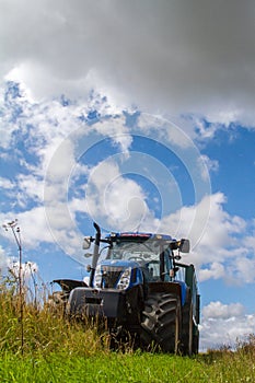 Modern blue tractor pulling a trailer in harvest field