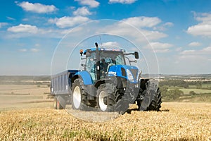 Modern blue tractor pulling a trailer in harvest field