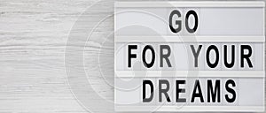 Modern board with text `Go for your dreams` on a white wooden background, top view. Overhead, from above, flat lay. Space for te