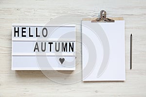 Modern board with text `Hello autumn`, noticepad with pencil. Top view