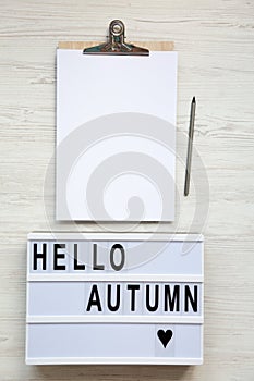 Modern board with text `Hello autumn`, noticepad with pencil. Top view