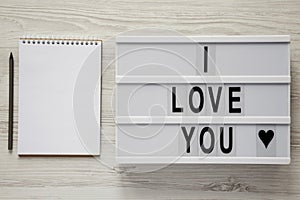 Modern board with text `I Love You`, notepad and pencil on a white wooden background, top view. Flat lay, overhead. Valentine`s