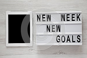 Modern board with text `New week new goals`, tablet over white wooden background, top view. From above, flat lay, overhead