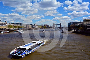 Modern boat on River Thames and Tower Bridge and HMS Belfast in the background, London, United Kingdom