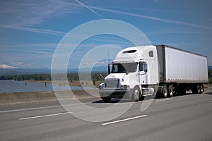 Modern bonnet white big rig semi truck with semi trailer driving