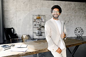 A modern Brazilian businessman stands poised with his laptop, his smart attire and relaxed demeanor