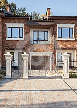 Modern brick house with plastic windows, modern wrought-iron gates and chimney.