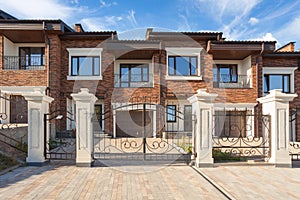 Modern brick house with plastic windows, modern wrought-iron gates and chimney.