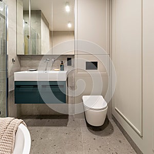 Modern bright bathroom with beige wall. Washbasin with turquoise cupboard and mirror. Wall with molding