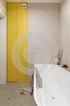 Modern bright bathroom with lamella wall. Big white bath with brown towel and orchid photo