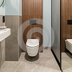 Modern bright bathroom with white toilet seat on wooden lamela wall. Mirror on grey wall