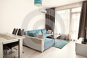 Modern bright and cozy living room interior design with sofa, dining table and kitchen. Grey and turquoise blue studio apartment