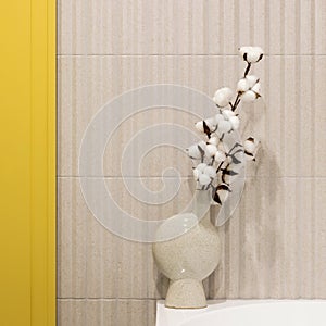 Modern bright and yellow bathroom with lamella wall. Big white bath with brown towel and dried flowers