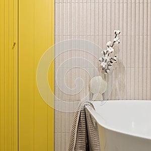 Modern bright and yellow bathroom with lamella wall. Big white bath with brown towel and dried flowers photo