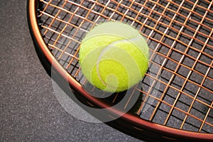 Modern brown tennis racquet with yellow ball on the strings