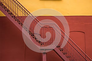 Modern building is burgundy yellow with an emergency exit fire metal staircase on the facade. Conceptual background