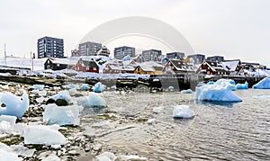 Modern buildings and small cottages with icebergs drifting in the lagoon, Nuuk old city harbor, Greenland