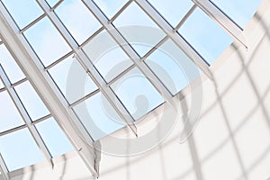 Modern builduing interior. Glass ceiling or steel structure in shopping mall. Blue sky on background. Glass roof, view fron inside