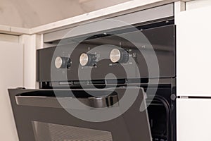 Modern built-in kitchen oven with open door and control knobs