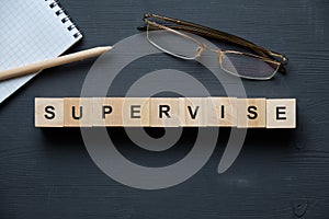 Modern business buzzword - supervise. Top view on wooden table with blocks. Top view