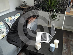 Modern business caucasian woman frustrated, crying, sitting on the sofa with a laptop and a cup of coffee