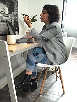 Modern business caucasian woman looking at her nails bored, she has a laptop, a cup of coffee and notes on her desk