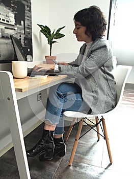 Modern business caucasian woman looking something on her phone and writing on her laptop, she has a cup of coffee and notes in her