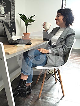 Modern business caucasian woman smiling and looking something on her laptop with a cup of coffee in her hand