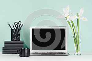 Modern business interior - workplace with blank computer display, black stationery, books, coffee cup, white spring bouquet.