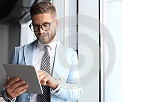 Modern business man in formalwear using digital tablet while standing near window in the office