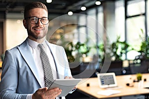 Modern business man in formalwear using digital tablet while standing near window in the office